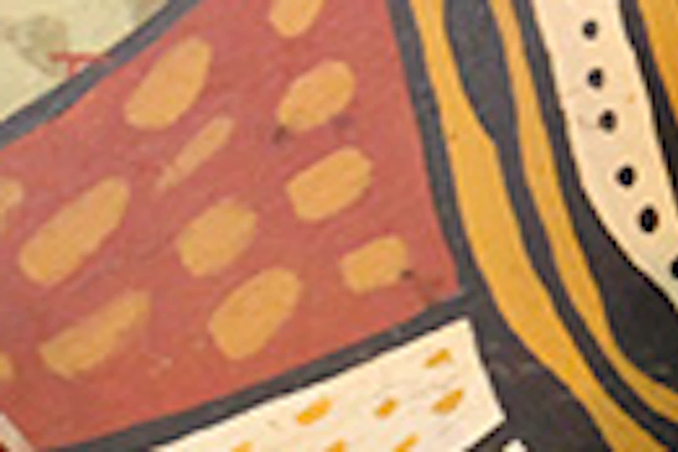 A person playing a didgeridoo while another person kneels beside them, holding a similar instrument, in front of an Indigenous art mural.