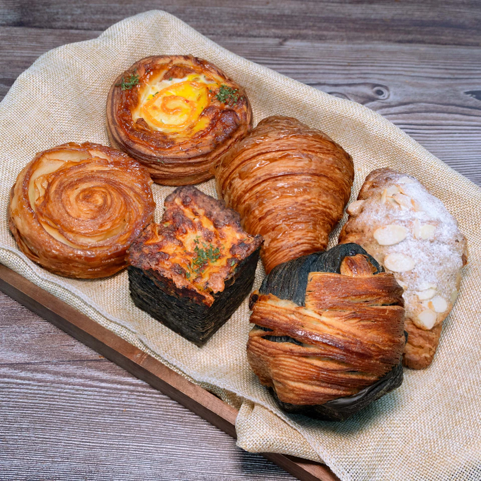 A selection of pastries displayed on a cloth-lined tray, including croissants, danishes, and a cube-shaped pastry.