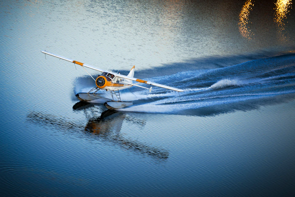 A seaplane with yellow and white colors skimming over calm water, leaving a wake behind.