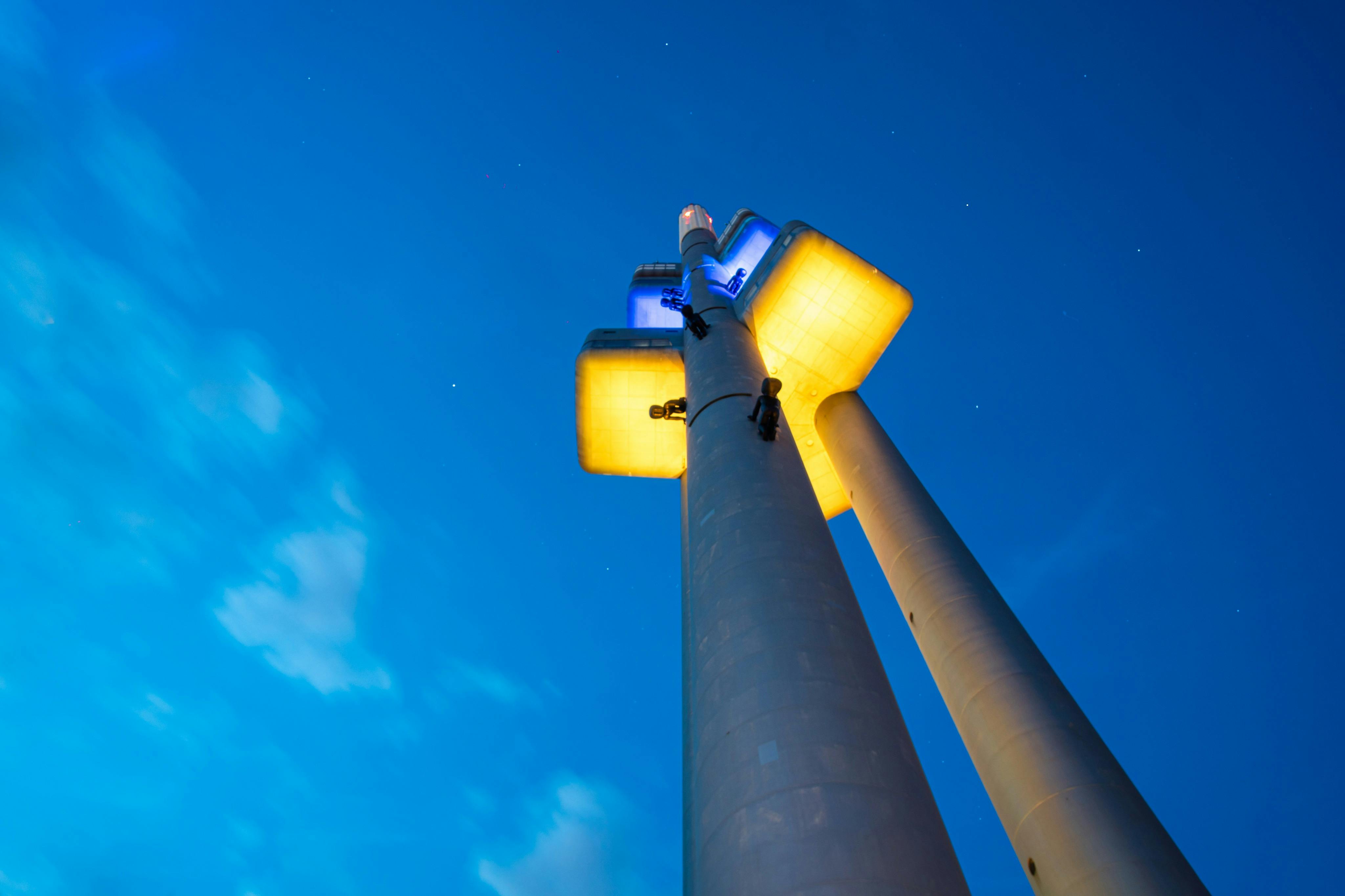 Une grande tour moderne avec des lumières jaunes et bleues sur fond de ciel bleu profond.