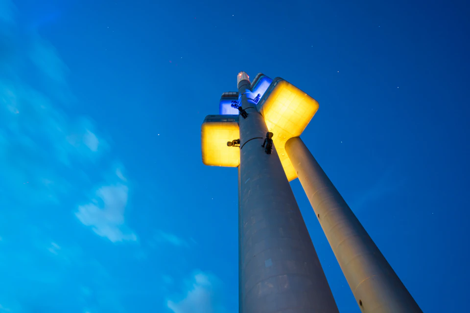 A tall, modern tower with glowing yellow and blue lights against a deep blue evening sky.