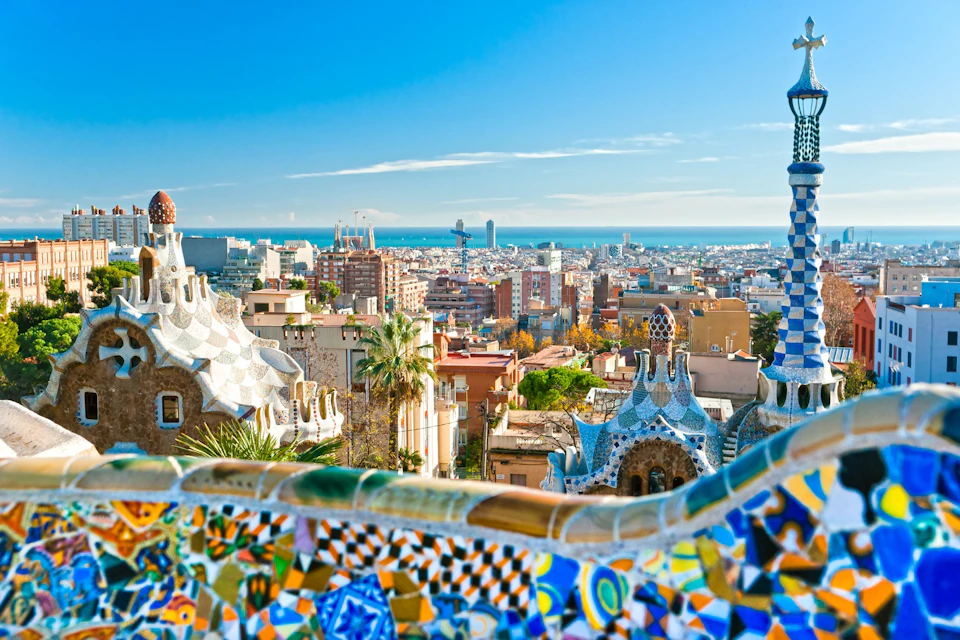 A vibrant cityscape with colorful mosaic structures in the foreground and a view of buildings and the sea in the background.