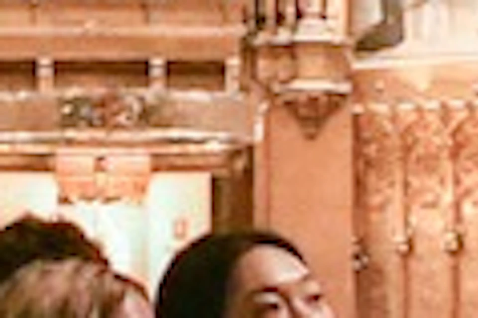 People walking inside an ornate church with arched ceilings, intricate decorations, and wooden pews.