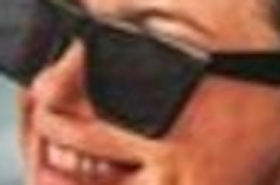 A person wearing sunglasses and a pink swimsuit sits on a red bench on a boat, smiling, with the ocean in the background.