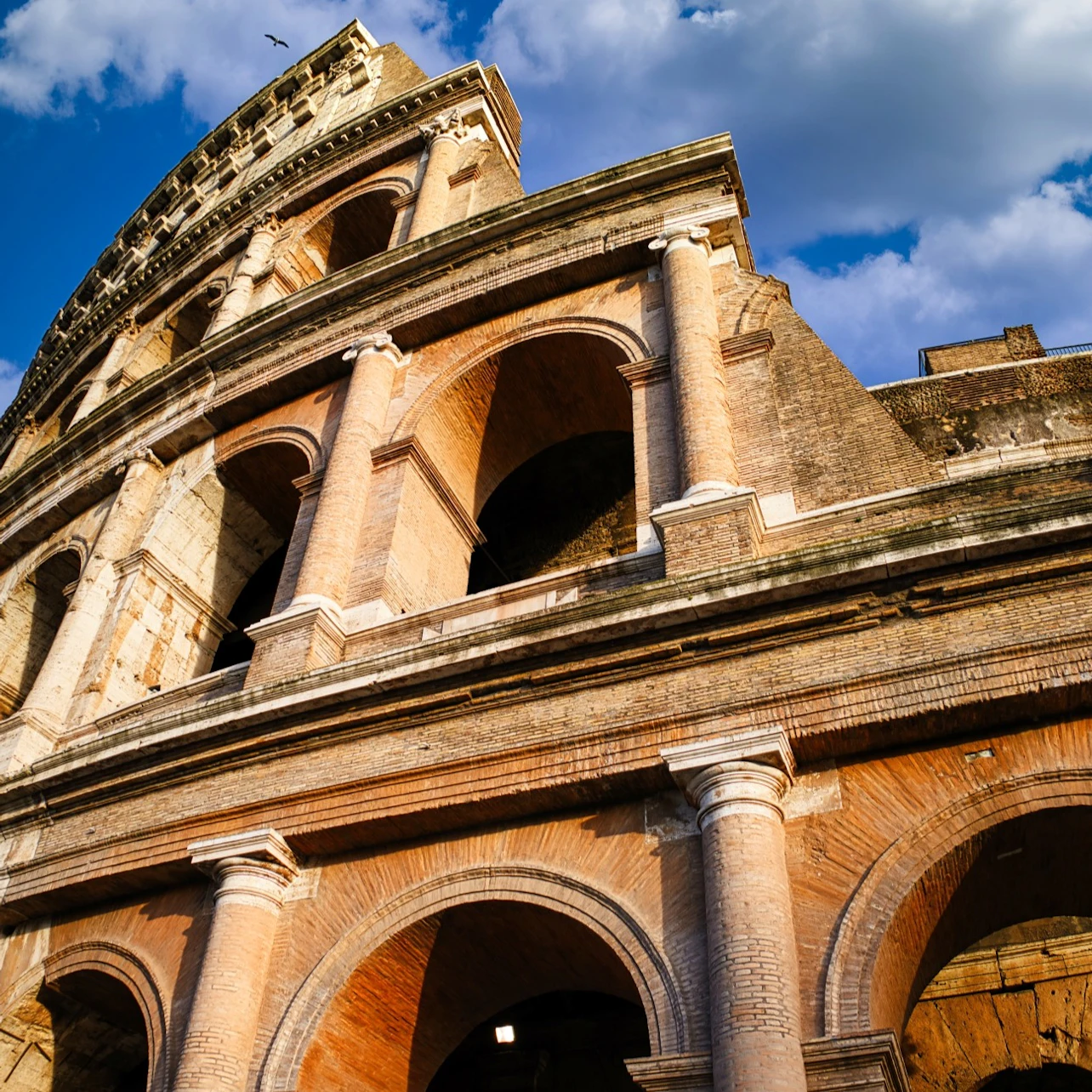 Upward view of the Roman Colosseum against a blue sky with clouds.