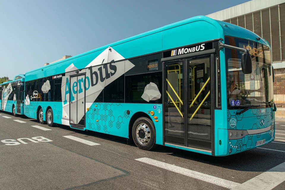 A turquoise bus labeled "Aerobus" with "Monbus" on the side, parked on a concrete surface next to a building.