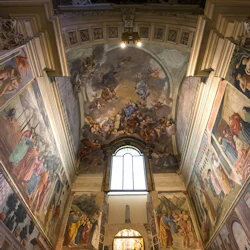 Ett katedraltak utsmyckat med detaljerade freskomålningar som visar olika religiösa scener och figurer, centrerade kring ett stort fönster.