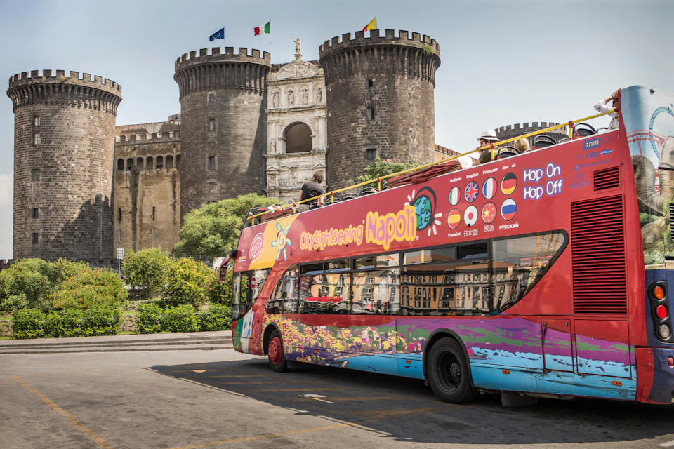 A City Sightseeing tour bus near a historic stone castle with cylindrical towers on a sunny day.