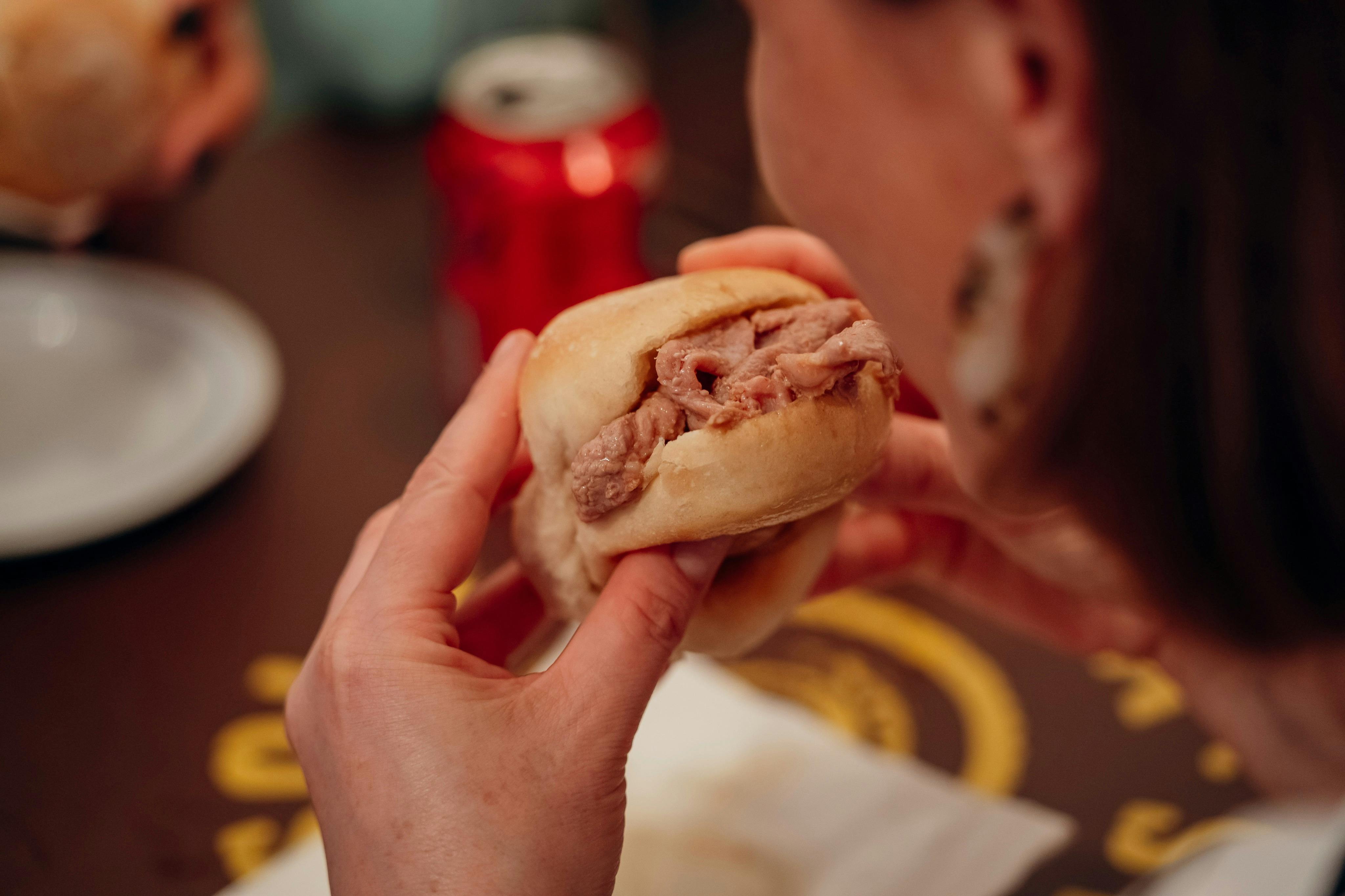 Nahaufnahme einer Person, die ein Roastbeef-Sandwich in der Hand hält und gerade essen will, mit sichtbaren Händen und einer unscharfen Limonadendose im Hintergrund.