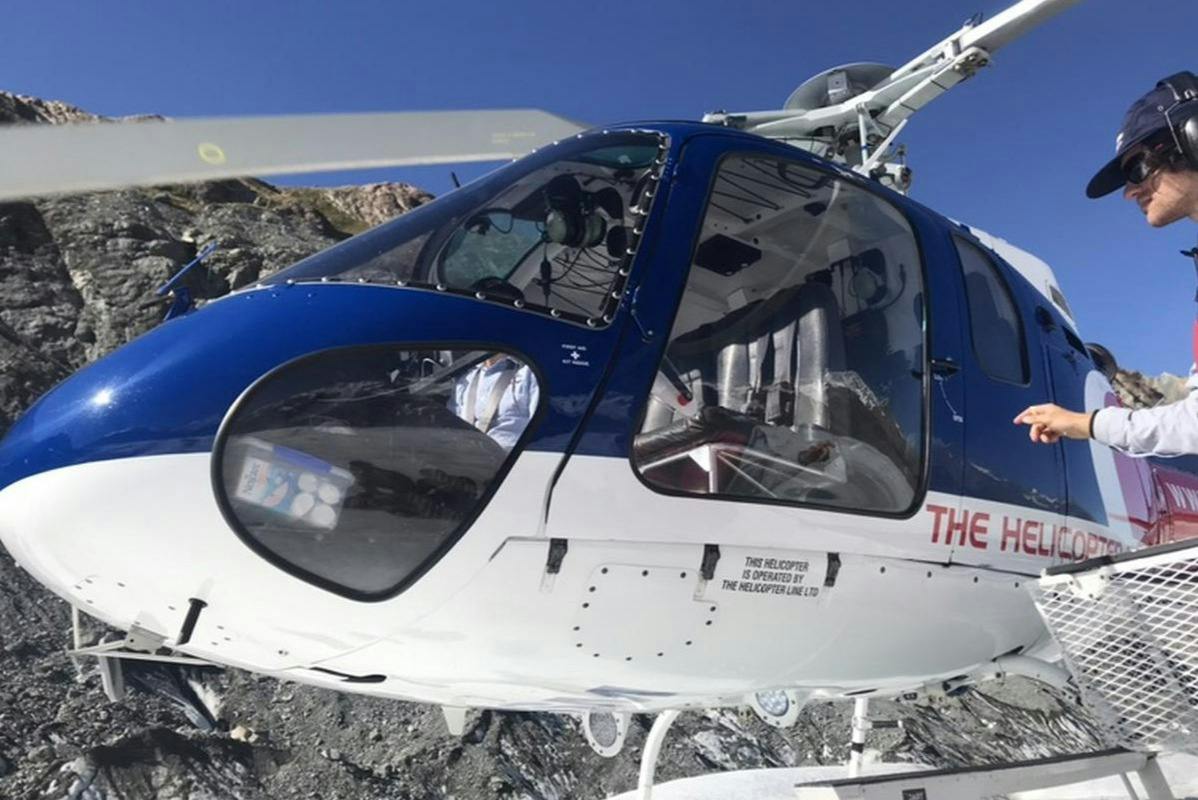 Close-up of a blue and white helicopter cockpit with visible interior and external details, set against a clear sky.