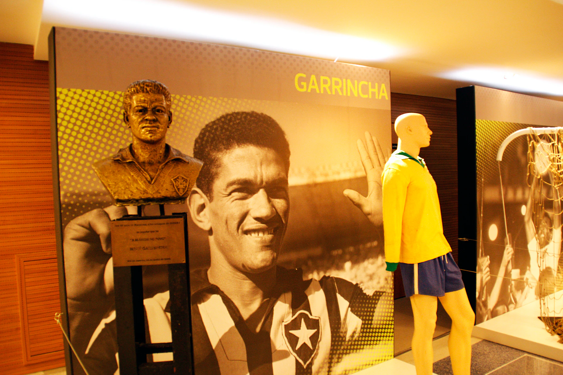 A bronze bust of Garrincha in front of a large photo of him smiling in a soccer jersey.