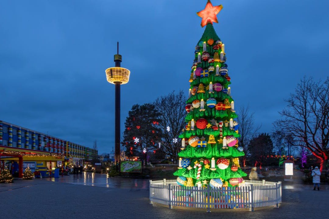 黄昏时分，公园里的一座塔楼旁边矗立着一棵大型圣诞树，上面装饰着五颜六色的装饰品和一颗星星。