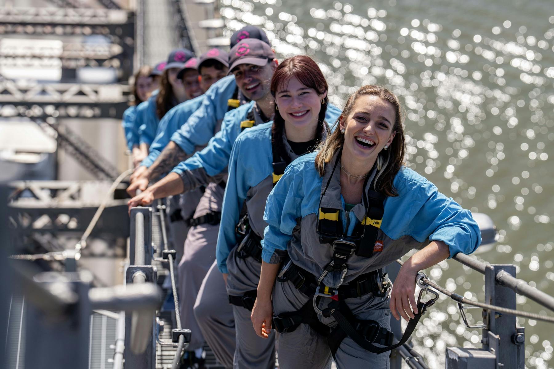 一群穿着安全装备的微笑者站在高架人行道上，后面有水。