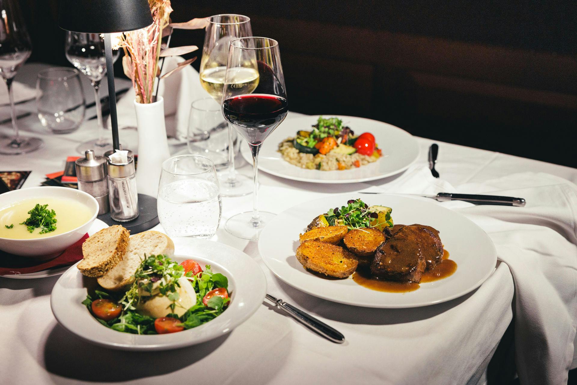 优雅的餐桌，配有白色桌布，配有餐盘、红葡萄酒、白葡萄酒和一杯水。
