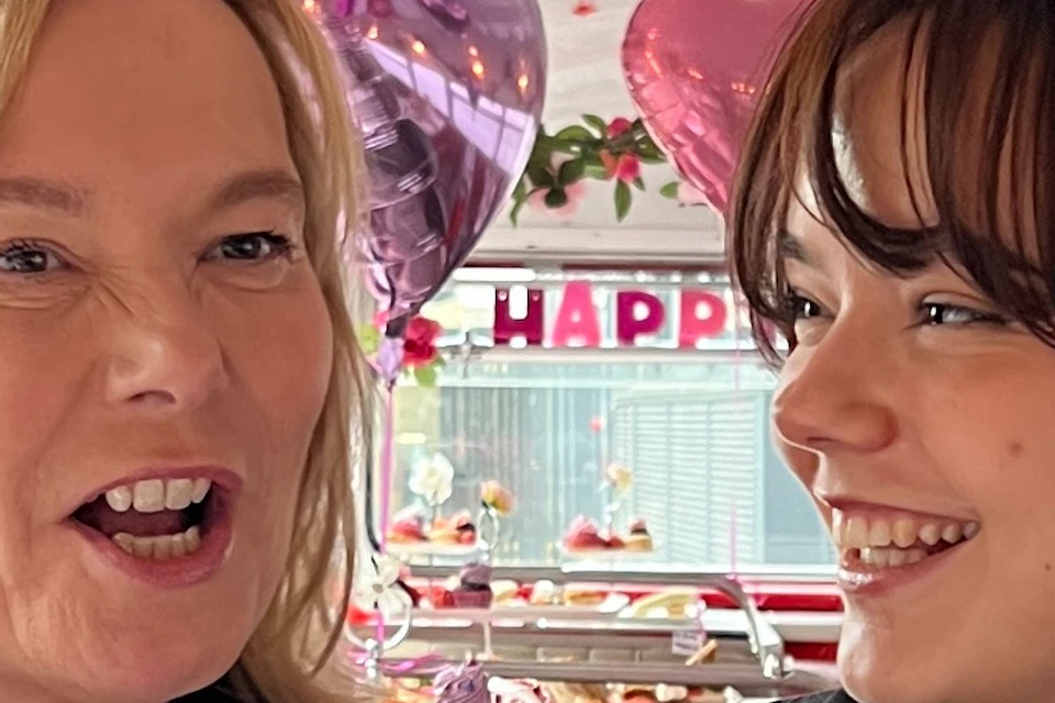 Two people smiling at each other in a festive setting with cupcakes and heart-shaped decorations.