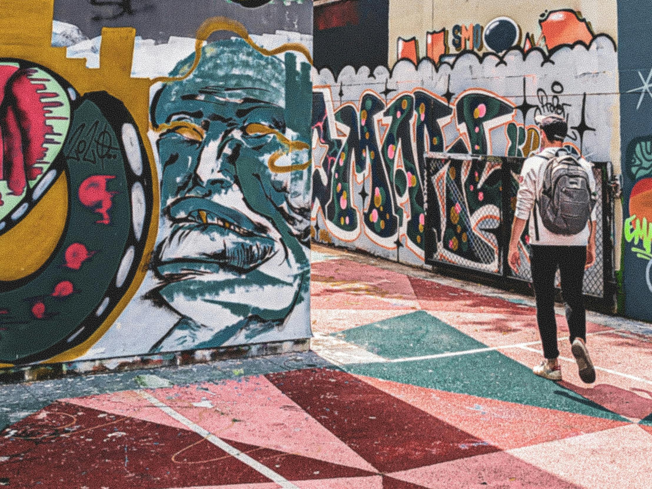 背着背包在五彩缤纷的地面上行走的人，周围墙上挂着充满活力的涂鸦艺术品。