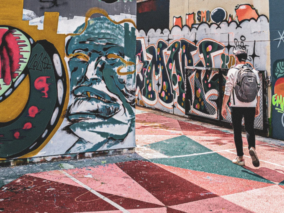 Person with a backpack walking on a colorful ground, surrounded by vibrant graffiti art on walls.