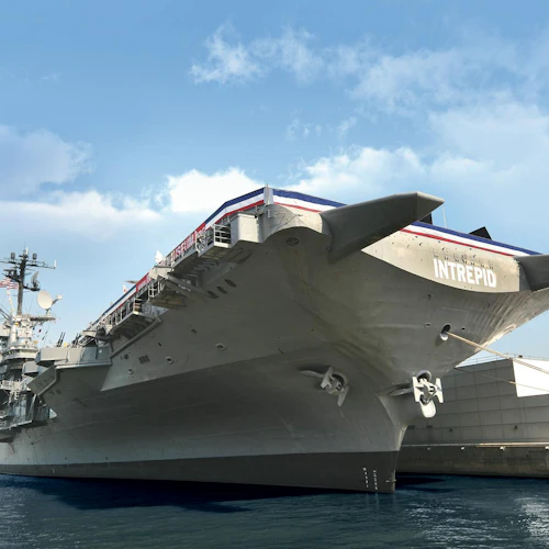 Großer Flugzeugträger Intrepid an einem Pier angedockt, vom Bug aus gesehen, unter einem teilweise bewölkten Himmel.