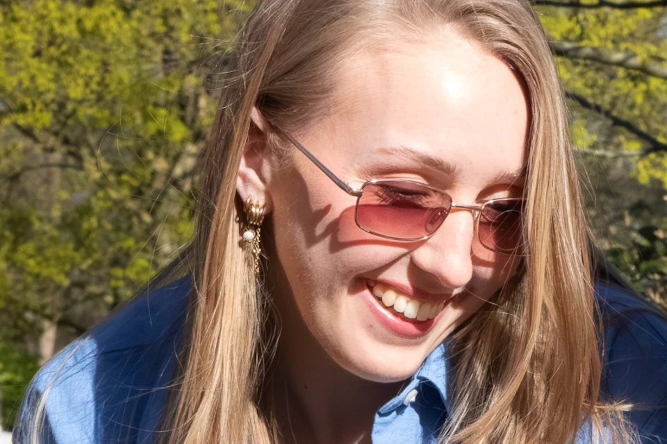 Two people smiling and looking at colorful tulips and daffodils in a garden on a sunny day, with trees in the background.