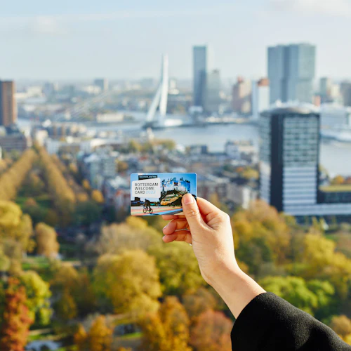 En hand håller ett "Rotterdam Welcome Card 2022" med panoramautsikt över Rotterdam i bakgrunden, med höga byggnader och en flod.