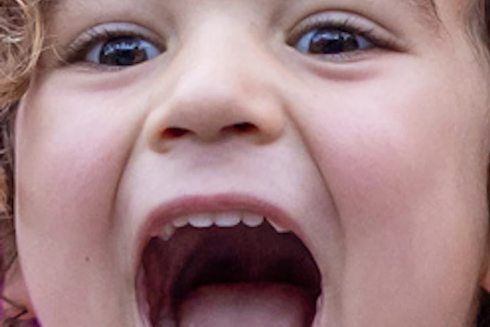 A young child with curly hair is excitedly holding a cookie, wearing an animal-themed shirt in a vibrant, colorful setting.