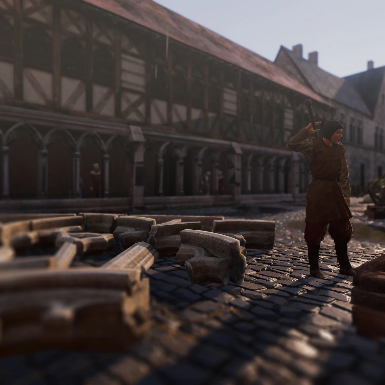A person stands on a cobblestone street near scattered stone blocks, in front of a medieval building with wooden beams and arches.