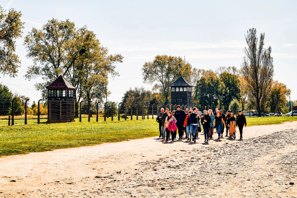 A group of people walking on a stone path surrounded by green grass and trees under a sunny sky.