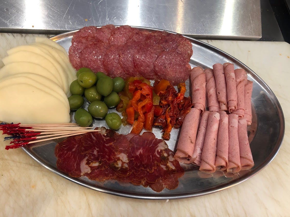 A platter of assorted cold cuts, cheese slices, green olives, and red pepper strips on a metal tray.
