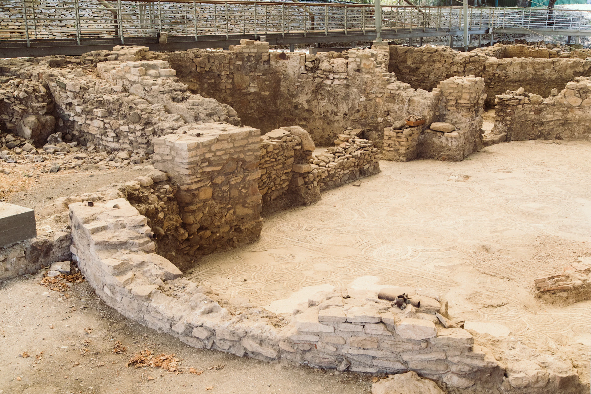 Ancient stone ruins with partially standing walls and a visible mosaic floor. Elevated walkway in the background.