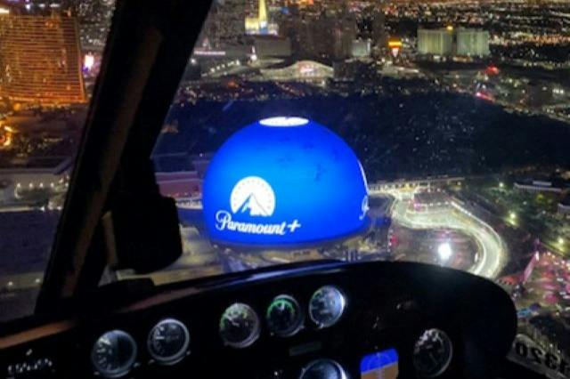 A nighttime view of a cityscape seen from an aircraft cockpit, featuring a large, illuminated blue dome with the Paramount+ logo.