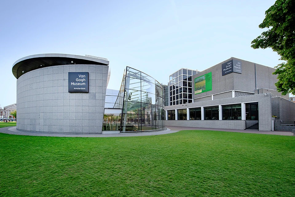 Van Gogh Museum exterior with modern architecture, glass entrance, and surrounding green lawn under a clear sky.