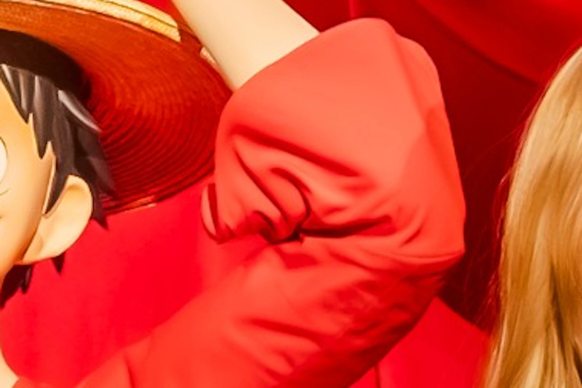 A person posing with two life-sized statues of anime characters against a red-curtained background, one of whom is holding a piece of meat.