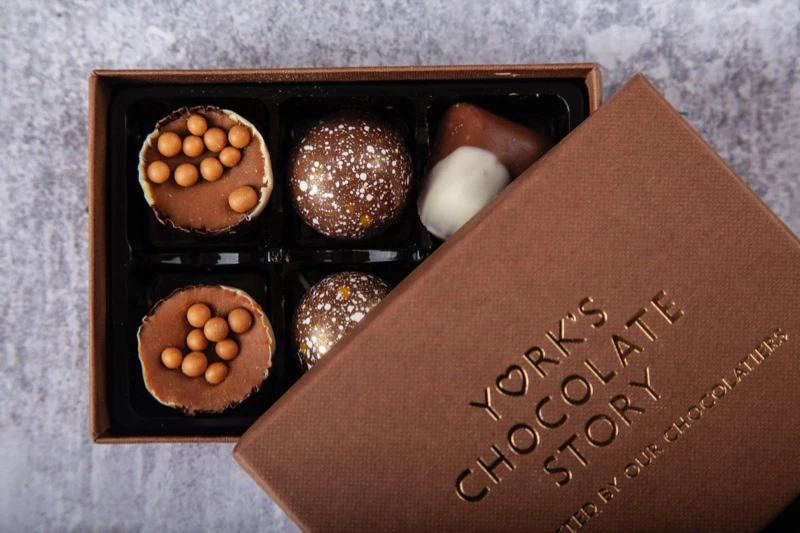 Box of assorted chocolates partially opened, revealing four chocolates with various toppings and one dipped in white and brown chocolate.