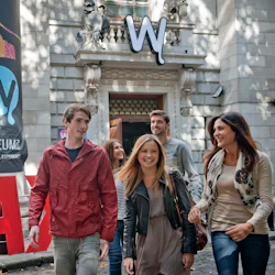 En grupp på fyra personer ler och går utanför National Wax Museums entré, med en stor "W" -skylt ovanför dörren.