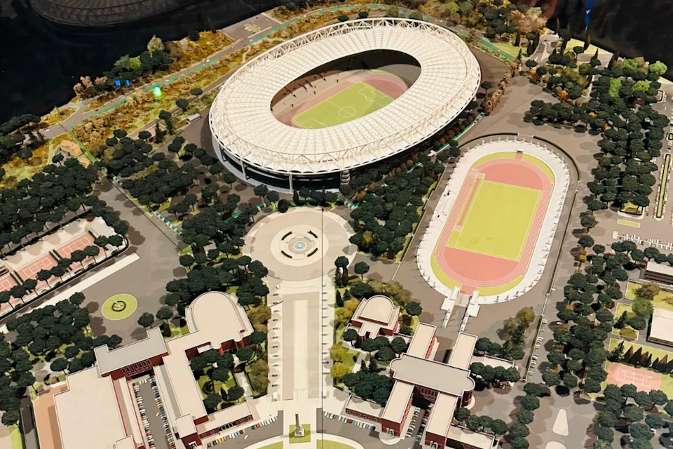 A detailed scale model of an urban sports complex featuring a large stadium, a smaller track and field area, and surrounding buildings.