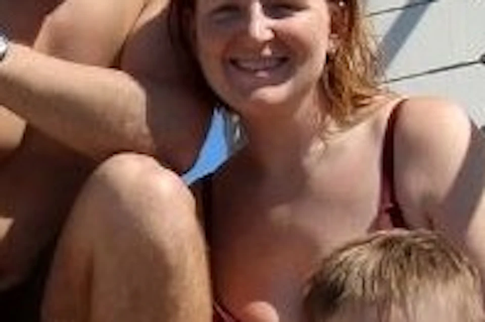 A family of four sitting on a boat's swim platform, smiling, with a clear blue sky and water in the background.