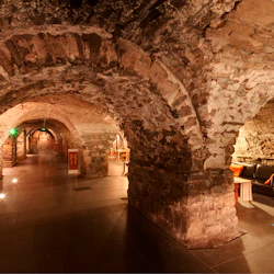 En svagt upplyst stengångskorridor med synliga tegelväggar, en svart soffa med kuddar och ett litet bord till höger.