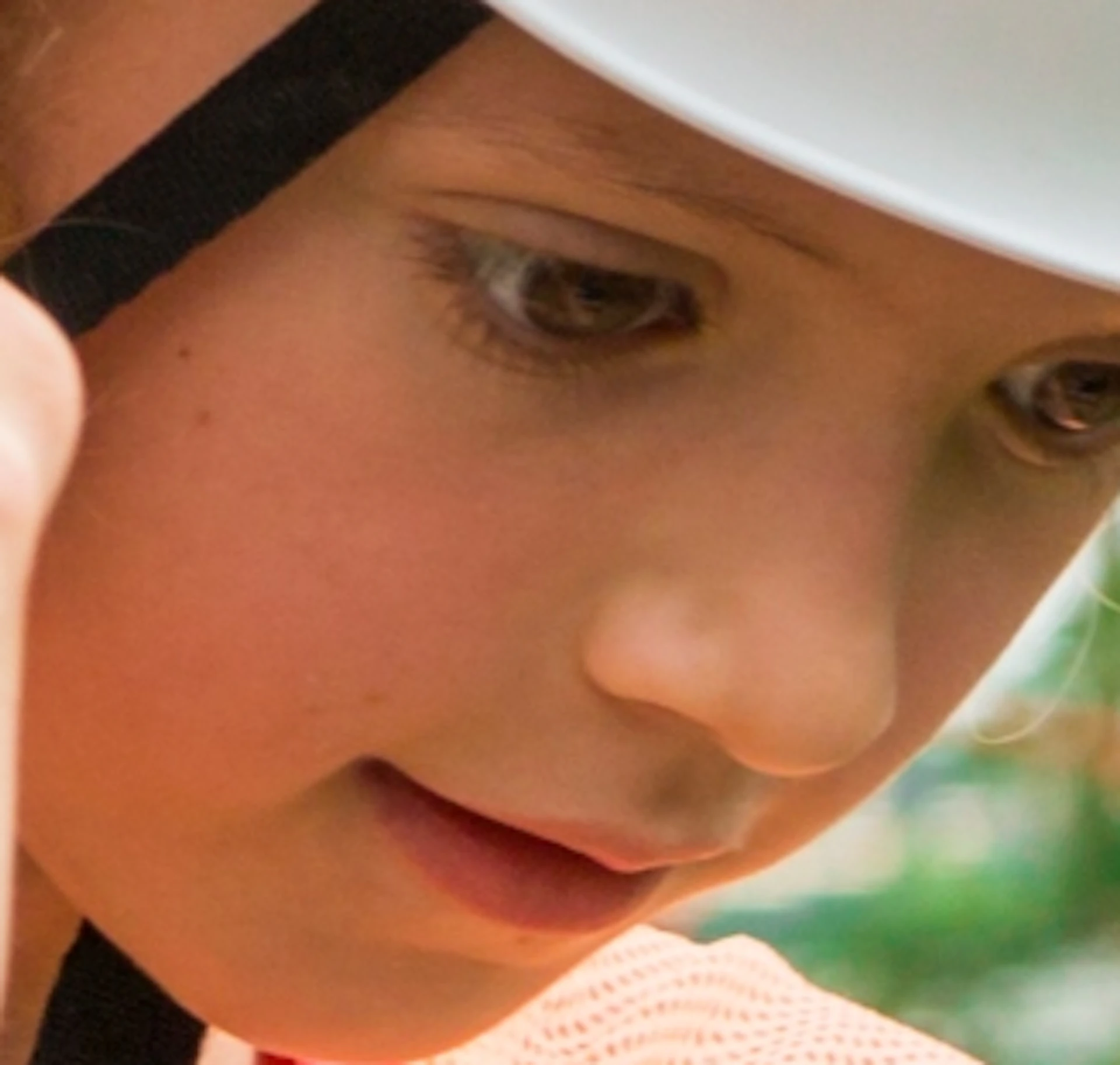 A child wearing a white helmet and harness navigates a ropes course outdoors, holding onto a red safety line.