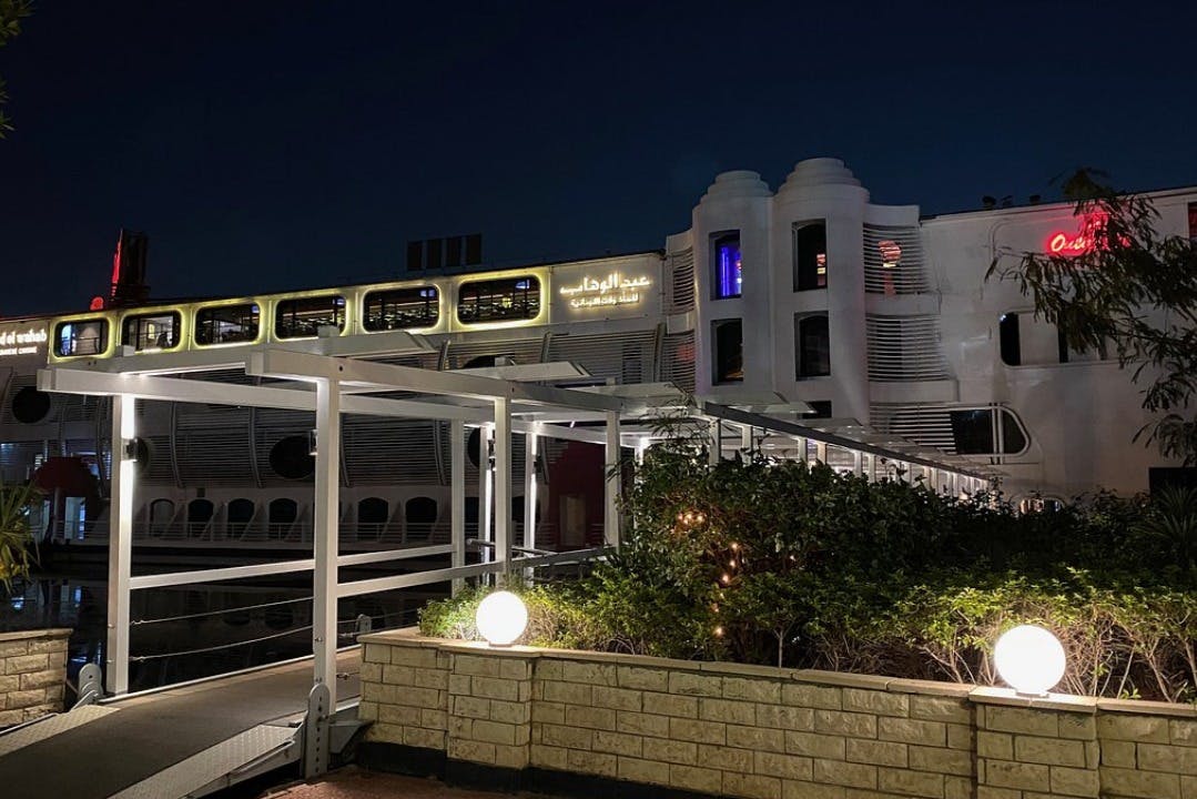 アラビア語の看板、夜間の設定、緑のある明るい通路、前景の明るい地球儀を備えたモダンな建物。