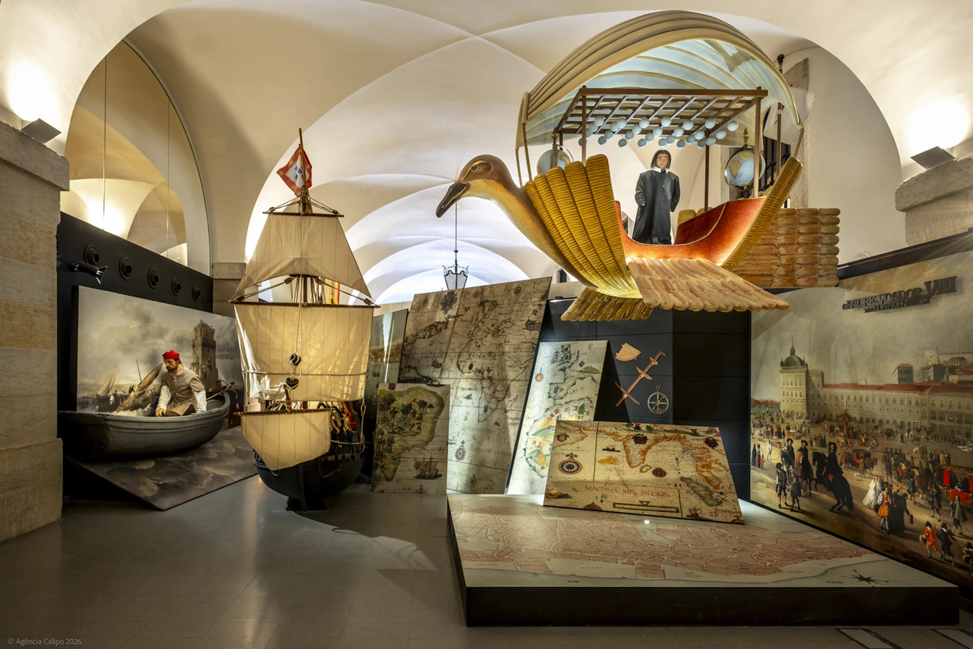 A museum exhibit showcasing historical maps, a sailing ship model, and a golden bird-shaped flying machine.
