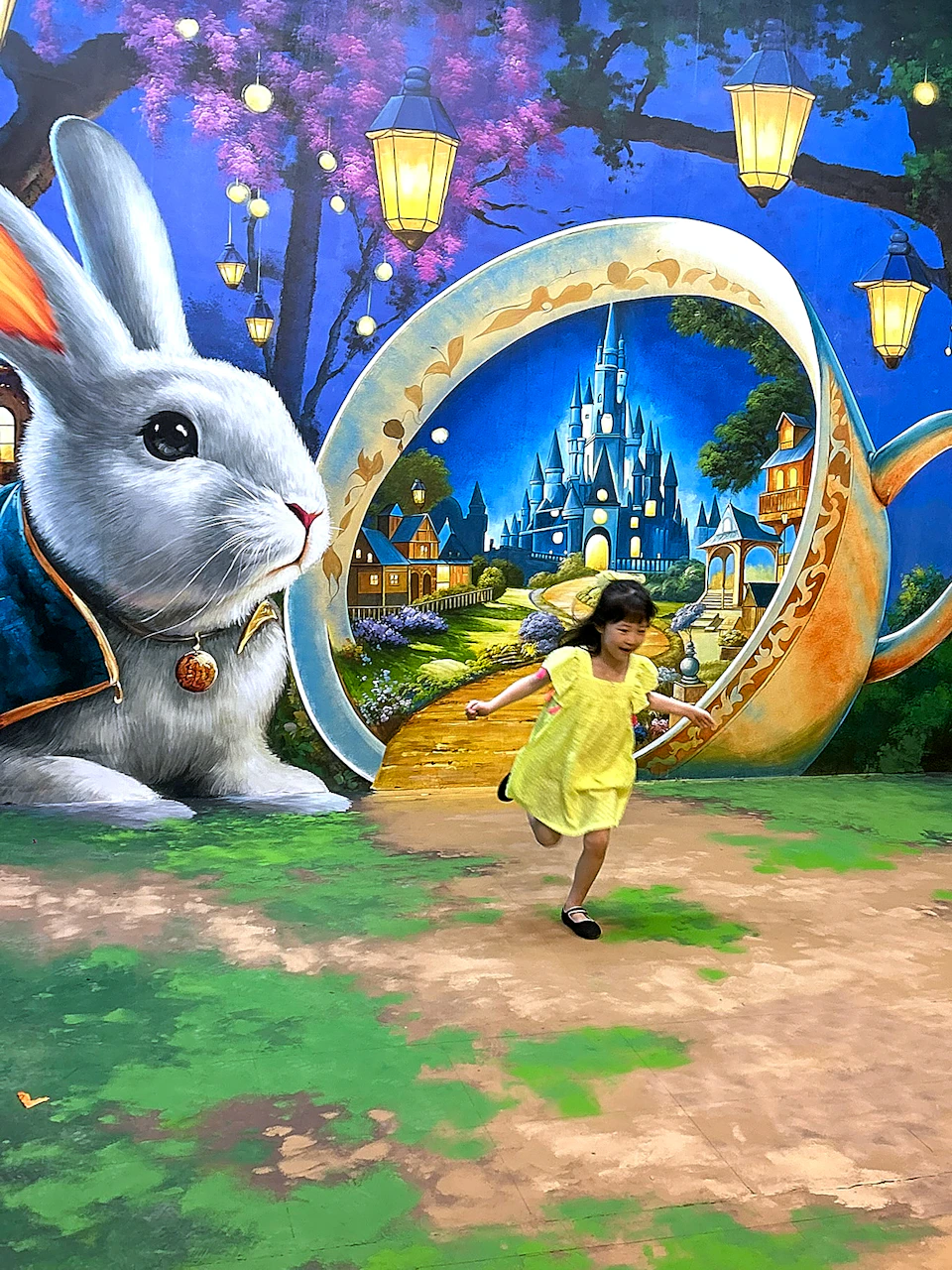 A girl in a yellow dress runs joyfully in front of a colorful mural featuring a rabbit and a fairytale castle in a teacup.