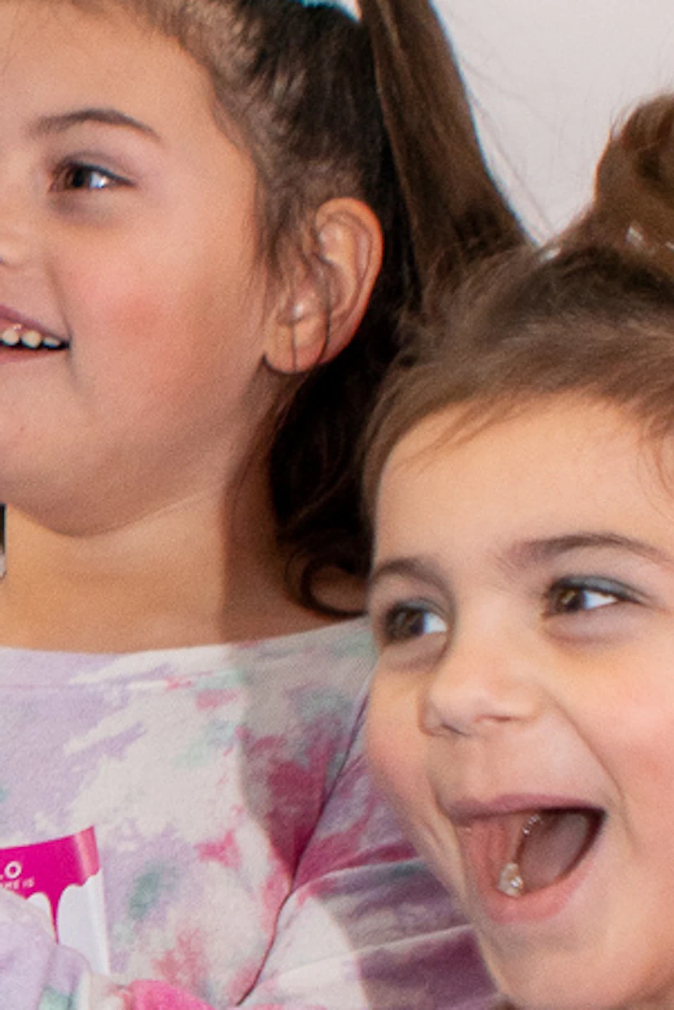 Two children wearing colorful shirts smile and play near a pink and yellow exhibit in a brightly decorated room.