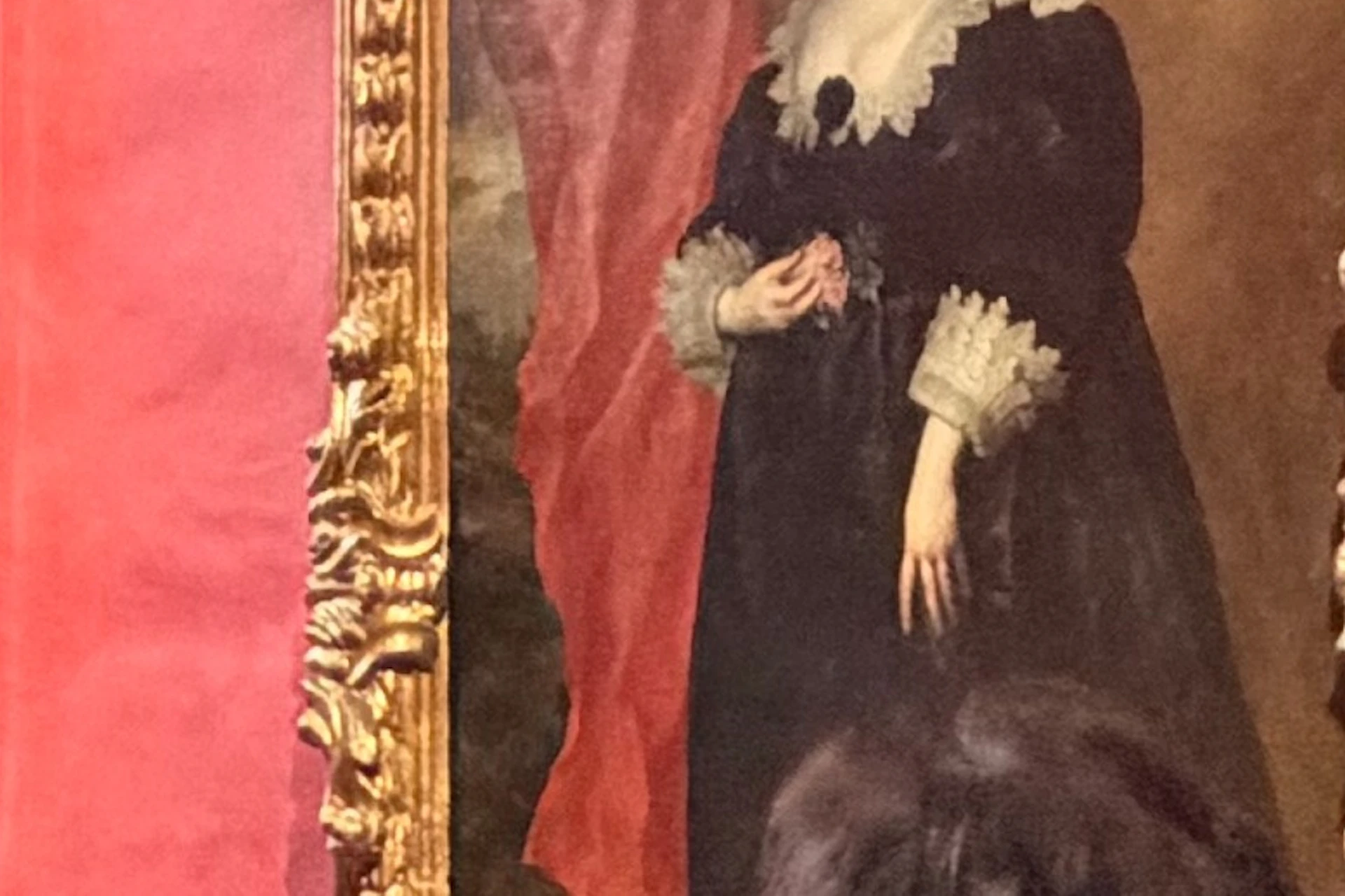 Visitors observing paintings in a red-walled museum gallery, featuring large, ornately framed portraits.