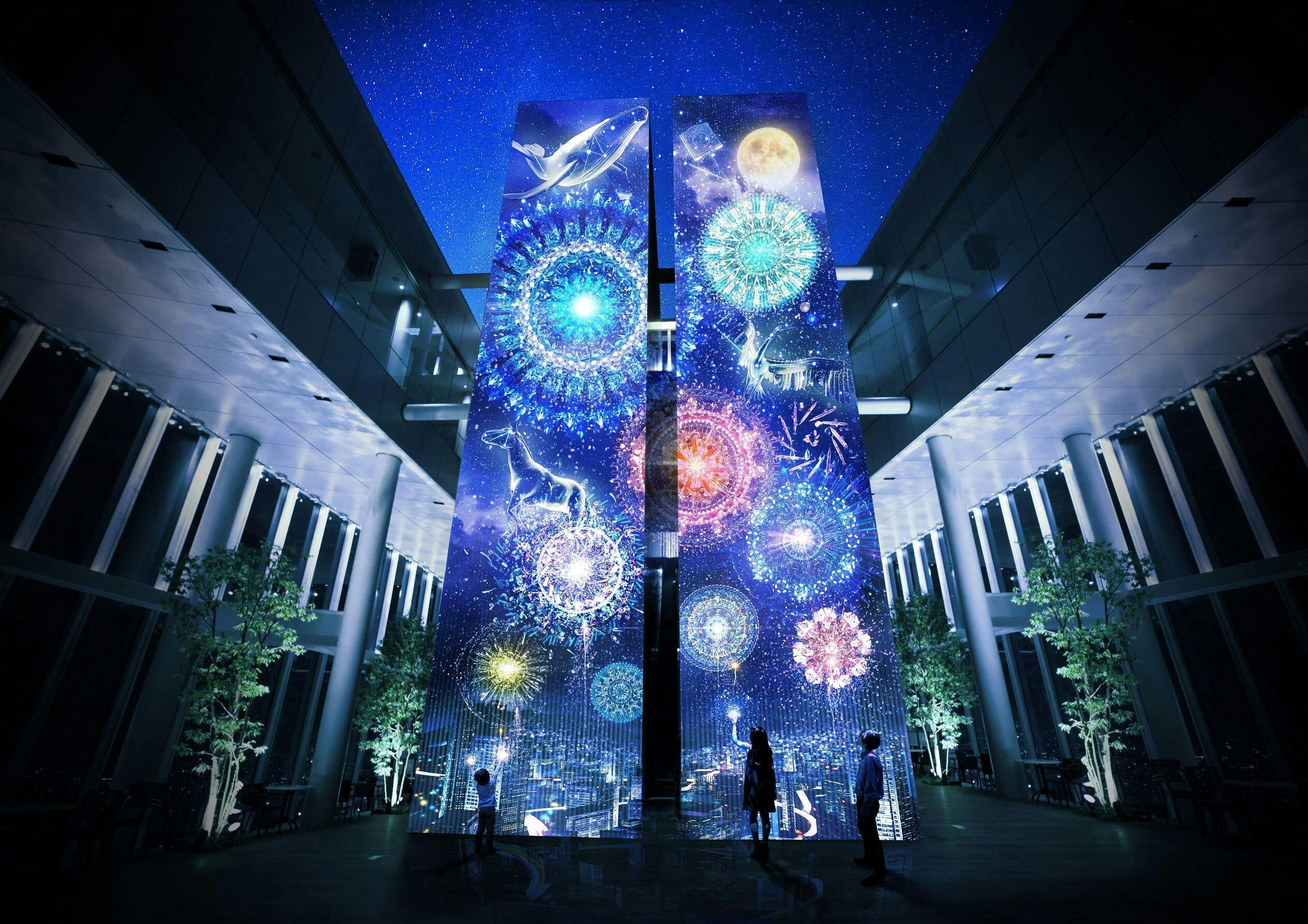 Vysoké digitální obrazovky zobrazují barevný ohňostroj a nebeské obrazy v moderním vnitřním prostředí. Displej sledují tři lidé.