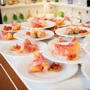 Plates of prosciutto-wrapped melon and bruschetta are neatly arranged on a table in a kitchen setting.