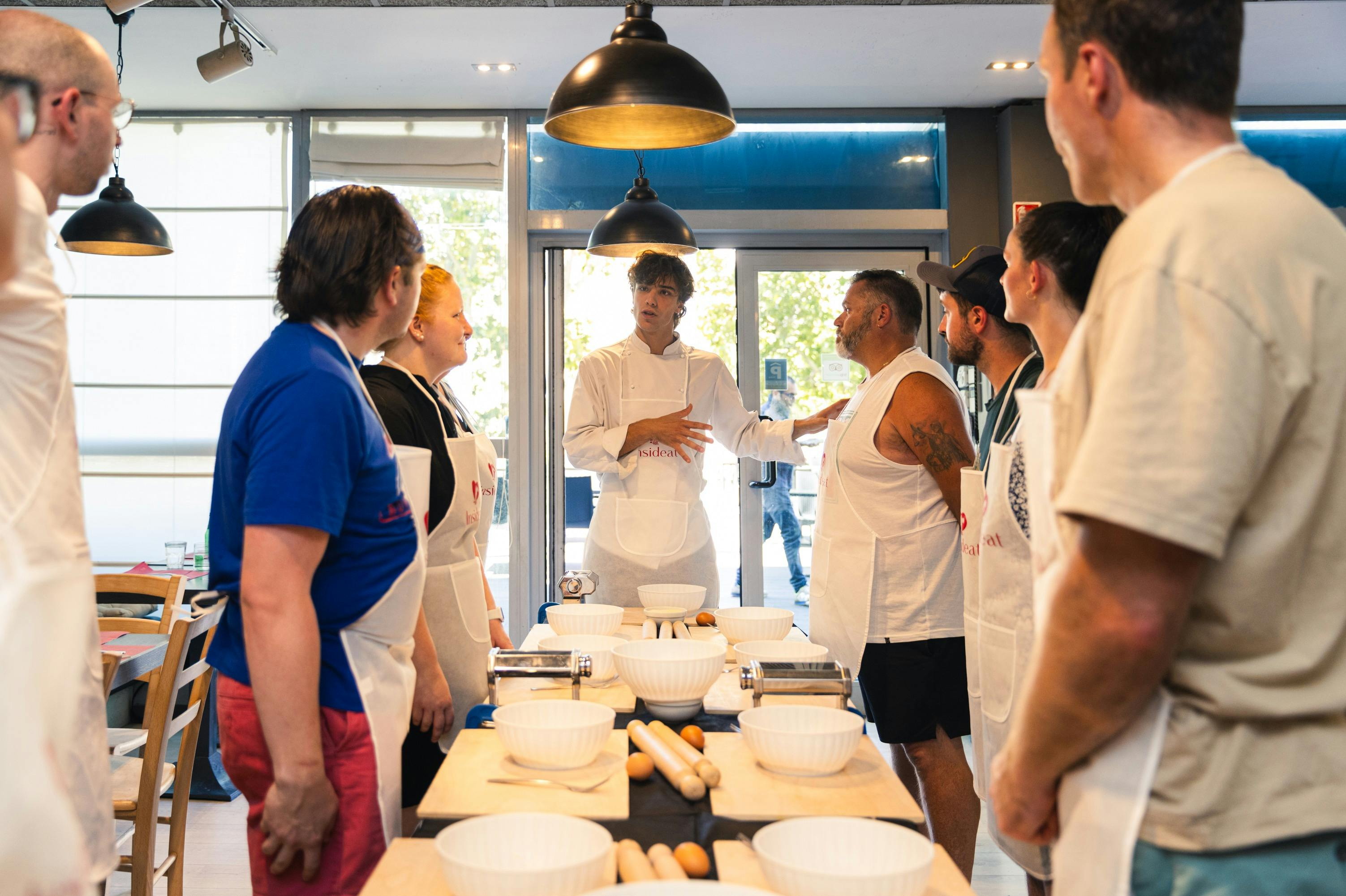 A cooking class scene with a group of people wearing aprons standing around a table with bowls and rolling pins.