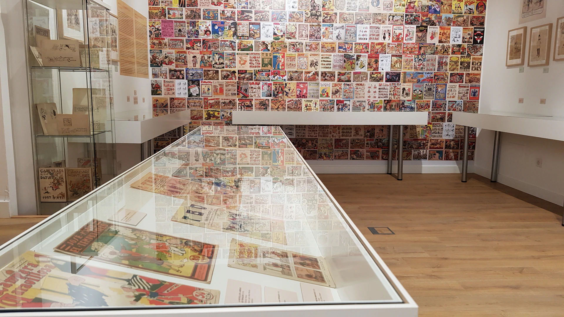 A display case with comic book pages, surrounded by walls covered in comic book artwork, in a well-lit exhibition space.