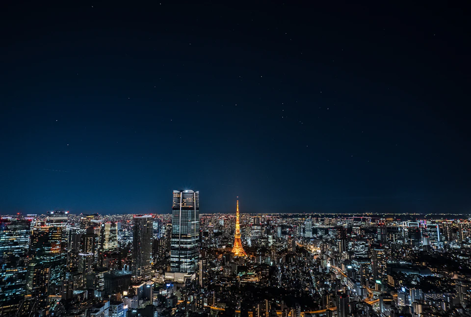 A cityscape at night featuring a brightly lit tower and skyscrapers under a clear, starry sky.