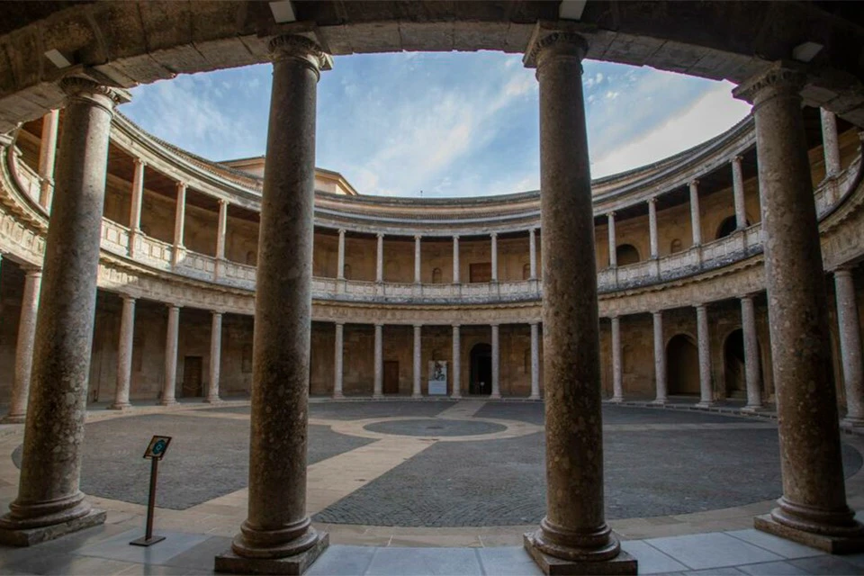 Circular stone courtyard surrounded by columns and arches, with a clear blue sky visible above.