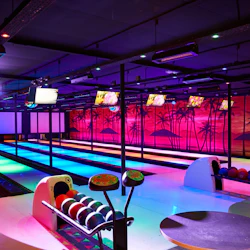 En livlig bowlinghall med neonbelysta banor, tropisk väggmålning, bowlingbollar och överliggande skärmar som visar grafik.